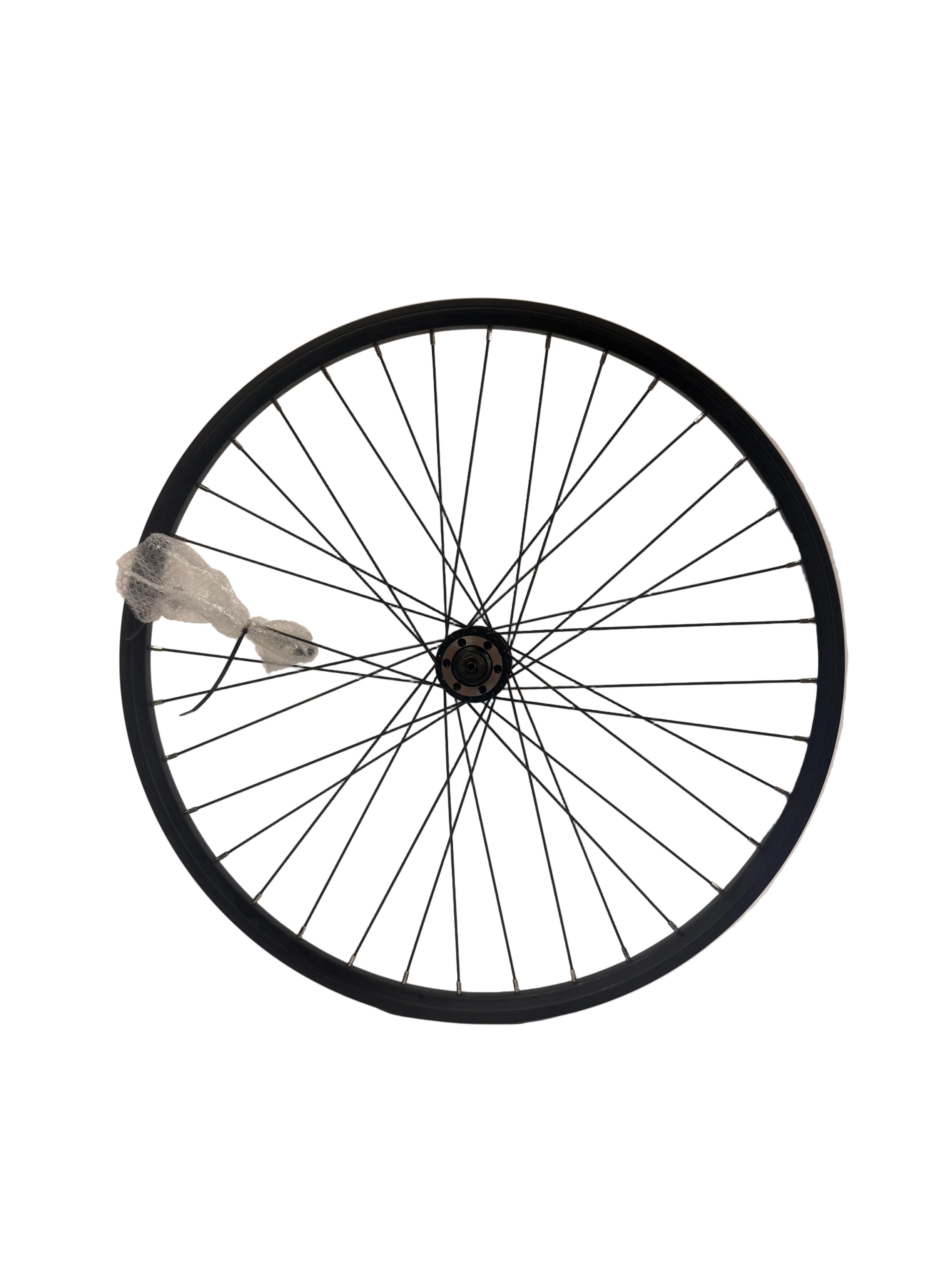 A black bicycle wheel with thin black spokes and a black hub, photographed against a plain light studio background. A small piece of clear plastic wrapping the skewer is attached near the outer left side of the rim.
